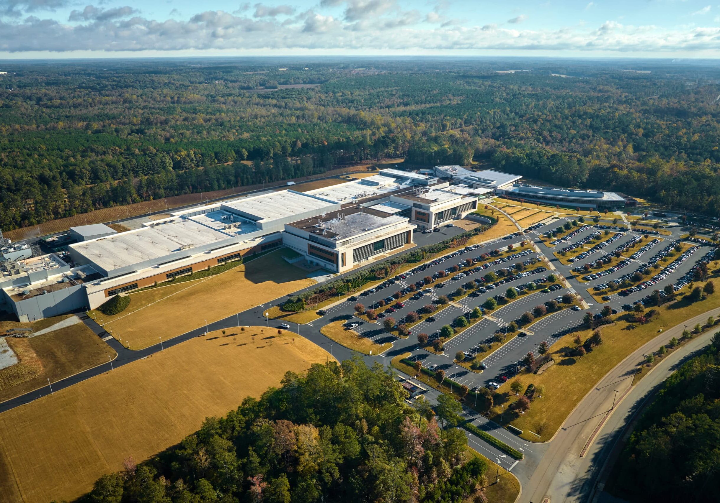 Aerial view of many employee cars parked on parking lot in front of industrial factory building.